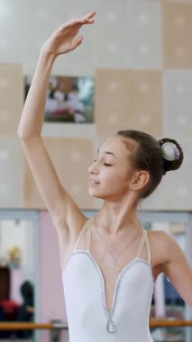 Bale salonunda, beyaz bale etekli kız, bale yapıyor, sütyen bölümünün provasını yapıyor, zarif bir şekilde elini kaldırıyor ve indiriyor, koridordaki korkulukta duran genç balerin...