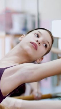 Bale salonunda genç balerin mor tek parça streç giysi içinde bir yamaç gerçekleştirmek geri viraj, geri, Korkuluk, hall, zarif yukarı ve aşağı, ayakta el hareketli yatır. yakın çekim.