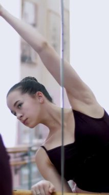 dans salonu, siyah tek parça streç giysi içinde genç balerin gerçekleştirmek yamaç kıstır, zarif eller taşıyarak, barre adlı bale sınıf aynada yakın duran.