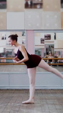 Dans salonunda, siyah taytlı genç balerin, bale sınıfında, büyük battement geri performans sergiliyor, bacağını zarif bir şekilde kaldırıyor...