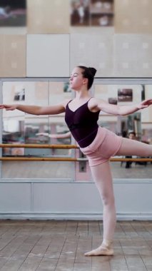 Dans salonunda, siyah taytlı genç balerin 1 arabesk performansı sergiliyor, bale sınıfında aynanın yanında, zarif bir şekilde bacağını kaldırıyor...