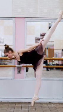 dans salonu, mor tek parça streç giysi içinde genç balerin zarif bir belirli bale egzersiz, Arabesk barre adlı bale sınıf aynada yakın duran Slope'da gerçekleştirir..