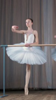 Eski tiyatro salonunda bale provası. Beyaz etekli genç balerinler, bale etekleri giyiyorlar, bale yapıyorlar, zarif bir bale egzersizi yapıyorlar, pas veriyorlar, barın yanında duruyorlar..