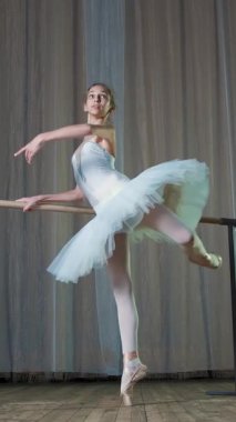 eski tiyatro salonunda bale prova. Genç balerin beyaz bale etekle tutu, meşgul balede, zarif gerçekleştirir belirli bir bale egzersiz, tutum allonge, barre duran.