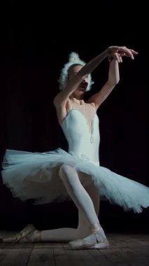 spot ışık, Sahne Alanı'ndaki eski tiyatro salonunun ışınları içinde. Beyaz Kuğu ve pointe ayakkabı, takım elbiseli genç balerin dans ediyor zarif belirli bale hareket, bölümü de sütyen.