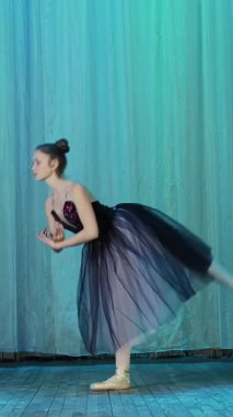 eski tiyatro salonu sahnesinde bale prova. Lila siyah elbise ve pointe ayakkabı, genç balerin zarif belirli bale hareket dans ediyor, onun bacak yükseltir yukarı arkasında.