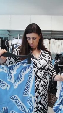 Alışveriş. Satın alma. Genç bir esmer kadın, mağazadan ya da pazar yerinden yeni şık kıyafetler seçiyor. Alışveriş merkezi. Moll. Süpermarket. İndirim, indirim.