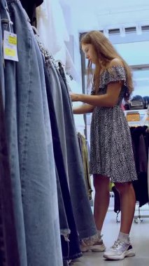 Alışverişe. Kıyafet alıyorum. Askıdaki giysiler. Alıcı giyim mağazasından alışveriş yapıyor. Kıyafet seçme süreci. Perakende. Satış. İndirim sezonu. mağaza..