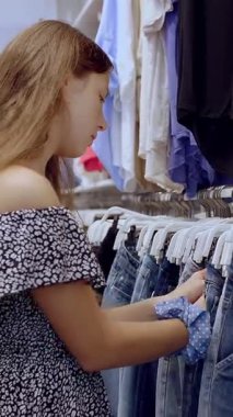 Alışverişe. Kıyafet alıyorum. Askıdaki giysiler. Alıcı giyim mağazasından alışveriş yapıyor. Kıyafet seçme süreci. Perakende. Satış. İndirim sezonu. mağaza..