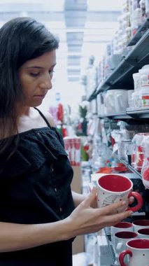 Bir süpermarkette ya da alışveriş merkezinde, genç esmer bir kadın Noel ve yeni yıl tatillerinde farklı ürünlere bakar. Noel için el sanatları. Noel ağacı aksesuarları.