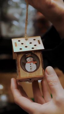 Noel süsleri. Şenlik aksesuarları. Yakın plan. İçinde kardan adam olan bir ev şeklinde Noel ağacı feneri. Noel Fuarı. Market ya da süpermarket raflarının bulanık arkaplanı. Mutlu Noeller ve mutlu yıllar..