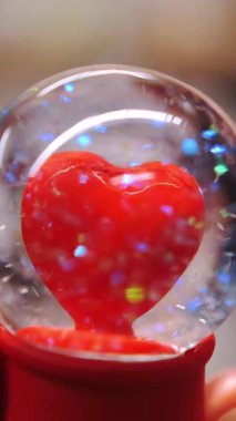 Sevgililer Günü. Yakın plan. Elimde. İçinde kırmızı bir kalp ve gökkuşağı parıltısı olan camdan bir top. Sevgililer Günü için romantik bir hediye. Şenlikli dekorasyon, Sevgililer Günü için dekorasyon. Aşk konsepti.