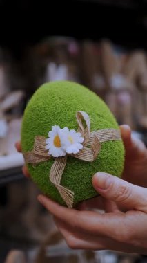 Paskalya panayırı. Yakın plan. Kadın elleri komik yeşil bir Paskalya yumurtası heykelciği tutuyor. Geleneksel Avrupa paskalya dekorasyonu ve dekorasyonları. Paskalya alışverişi, mağazada vitrin..