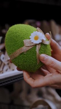 Paskalya panayırı. Yakın plan. Kadın elleri komik yeşil bir Paskalya yumurtası heykelciği tutuyor. Geleneksel Avrupa paskalya dekorasyonu ve dekorasyonları. Paskalya alışverişi, mağazada vitrin..