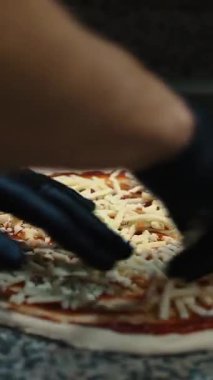 Pizza restoranın mutfağında hazırlanıyor. Şef İtalyan pizzasına peynir serpiyor..