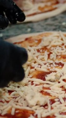 Pizza restoranın mutfağında hazırlanıyor. Şef İtalyan pizzasına peynir serper. Yakın plan yiyecek.