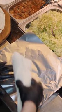 Şef şu malzemeleri kullanarak shawarma hazırlıyor: lavaş, et, sos, sebze, salatalık, soğan, lahana, baharatlı biber, patates, yeşillik, havuç