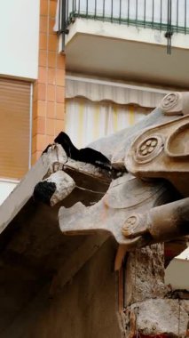 A hydraulic excavator with a demolition shear in action, tearing apart a building in an urban setting. the equipment is depicted amidst debris, urban renewal or redevelopment efforts