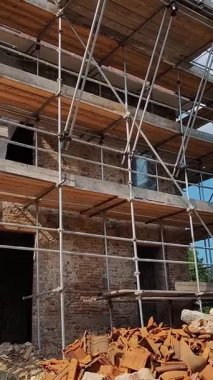 Güneşli bir günde İskele ve İnşaat Makineleriyle İnşaat Tamiratı. Yapının dış kısmında iskele ve enkazın ortasında bir inşaat kazıcısı var.