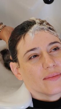 Kuaför boyamadan önce kadının saçını yıkar. Kuaför esmerin saçını yıkıyor. Siyah saçlı.