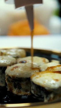 Suşi. Japon yemeği. Yemek pişirmek. Mutfak. Yakın plan. Suşi şefi taze pişmiş suşi rulolarına sos döküyor, siyah tabakta servis ediliyor. Bir restoranda sanat hizmeti. Asya yemekleri