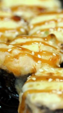 Suşi. Japon yemeği. Yakın plan. Siyah tabakta servis edilen taze pişmiş suşi ruloları dönüyor. Yemek pişirmek. Mutfak. Asya yemekleri