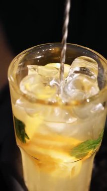 Kokteyl hazırlıyorum. Yakın plan. Barmen bütün malzemeleri ve buzları uzun bir kokteyl bardağıyla karıştırıyor..