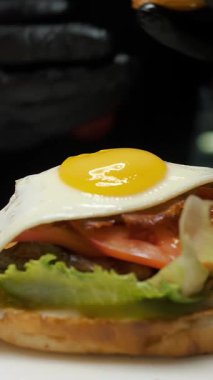 Hamburger. Yemek pişirmek. fast food. Aşçı yumurta burger yapıyor. Sosu, eti ve sebzesi olan sulu bir burger, üstünde kızarmış yumurta ve çıtır ekmek..