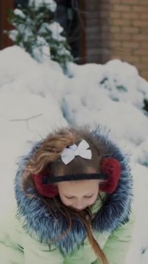 Kış manzarasının arka planında, kız bahçede karla oynuyor, fırlatıyor, karlara kürek serpiyor. Eğleniyor..