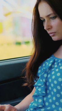 mavi elbiseli güzel esmer kadın arabada oturur, dizüstü bilgisayar, sosyal ağlarda iletişim çalışıyor. Internet, mobil iletişim kullanır