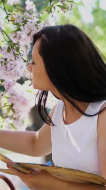 Beyaz elbiseli, sanatçı boya bir resim içinde çiçek açan çiçeklerin güzel kadın ressam bahar elma bahçesi, o bir palet boya ve bir fırça ile onun elinde tutan
