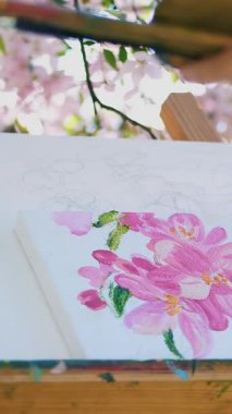 yakın çekim, ressam beraberlik çiçek dolu bir resim bahar elma bahçesi çiçek açan, fırça, tutar palet boya ile boyar. Rüzgar çiçekli dallar şövale üzerinde süpürür.