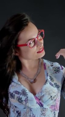 Kırmızı dudaklı esmer bir kadının portresi şık gözlük ve gözlük takıp stüdyoda poz veren. koyu gri arkaplan.