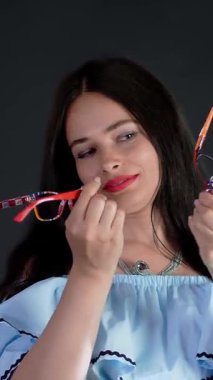 Kırmızı dudaklı esmer bir kadının portresi farklı gözlük, gözlük ve gözlük giyer ve stüdyoda kameraya bakar..