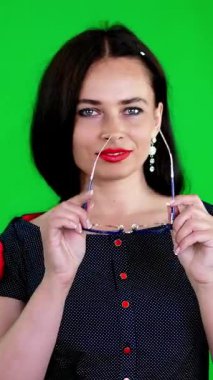 Kırmızı dudaklı esmer bir kadının portresi, şık gözlüklü, gözlüklü, eğlenceli hareketler yapan, kameraya bakan, stüdyoda poz veren. yeşil arka plan, kromeakey.