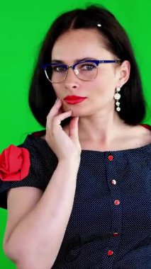 Kırmızı dudaklı esmer bir kadının portresi, şık gözlüklü, gözlüklü, eğlenceli hareketler yapan, kameraya bakan, stüdyoda poz veren. yeşil arka plan, kromeakey.