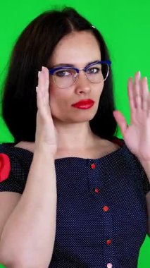 Kırmızı dudaklı esmer bir kadının portresi, şık gözlüklü, gözlüklü, eğlenceli hareketler yapan, kameraya bakan, stüdyoda poz veren. yeşil arka plan, kromeakey.