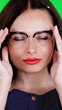 Kırmızı dudaklı esmer bir kadının portresi, şık gözlüklü, gözlüklü, eğlenceli hareketler yapan, kameraya bakan, stüdyoda poz veren. yeşil arka plan, kromeakey.