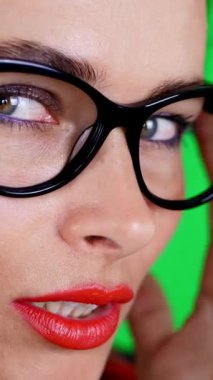 Kırmızı dudaklı esmer bir kadının portresi, şık gözlüklü, gözlüklü, eğlenceli hareketler yapan, kameraya bakan, stüdyoda poz veren. yeşil arka plan, kromeakey.