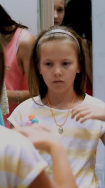 Alışverişe. Büyük bir mağazanın soyunma odasında, güzel, ciddi bir kız, bir çocuk yeni kıyafetler deniyor, ne alacağına karar veriyor. Aynadaki yansıma. Çocuk giyim departmanı. Küçük moda kızı..