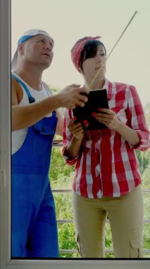 çekici inşaat işçisi ve güzel kadın Yardımcısı ölçümleri ölçüm bandı kullanarak Windows ve notları tablet içinde olun. hizmet adam yükleme penceresi .