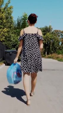 Arkadan görünüm, kız taşıyan bir paket çöp onun elinde, çöpü dışarı atma. yaz sıcak gün. ekoloji. enkaz, çevre temizliği ayrılması
