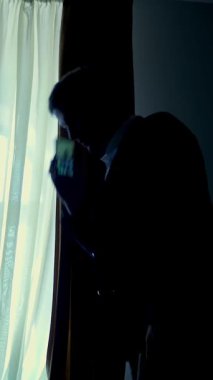 gece karanlığında, pencerenin karşısında karanlıkta. yakışıklı adam, bir smartphone cep telefonu üzerinde evde, onun yatak odasında konuşurken işadamı bir beyaz gömlek ve mavi ceket tutuyor