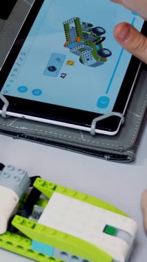 Yakın plan, tablet bir talimat gösteriyor, tasarımcıdan bir cihaz yaratmak için bir model. Okul çocukları, Robot Bilimleri ve Kök Eğitimi Okulu 'nda bir tasarımcıyla çalışıyor..