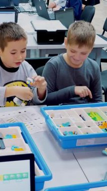 Öğrenciler, çocuklar, oğlanlar ve kızlar, tabletlerdeki çizimlere göre tasarımcı, demir olmayan parçalar, bloklar kullanarak cihazlar oluşturun. Robot Bilimi Okulu, Kök Eğitimi.