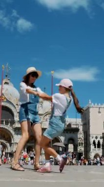  Mutlu güzel kadın ve çocuk manzarası, turistler, el ele tutuşmalar, San Marco Meydanı 'nda dönmeler, St Mark Bazilikası, bir yaz günü.