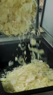 Yakın plan, eldivenli bir aşçı büyük endüstriyel kızartma tavasına bol miktarda taze soğan koyar. Kızartırken soğan karıştırır. Yemekhanede, restoranda yemek pişirme süreci.