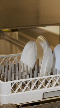 Kapatın, sanayi için otomatik bulaşık makinesinde beyaz tabak, mutfak kafeteryasında bulaşık makinesi, kantin, self-servis restoranı. Bulaşık yıkama işlemi, bulaşıklar bulaşık makinesinde yıkanır.