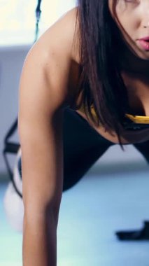 Yakın plan, portre, taytlı çekici esmer kadın, sarı bluz ve spor ayakkabılar, spor salonunda kemer takarak egzersiz yapıyor. Güzel, sportif, renkli vücutlu güzel bir kadın spor için içeri girer.,