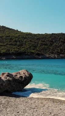 Yunanistan 'ın Evia Adası' nın güzel plajı. Deniz koyunda turkuaz, kayalıkların dibinde mavi su, dağların arasında. Denizde beyaz köpüklü yumuşak dalgalar Yazın sıcak güneşli günü